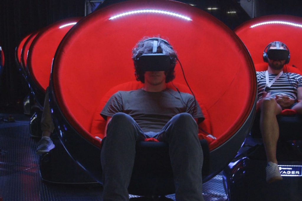 Two people sitting inside of Voyager motion chairs watching a program in VR.