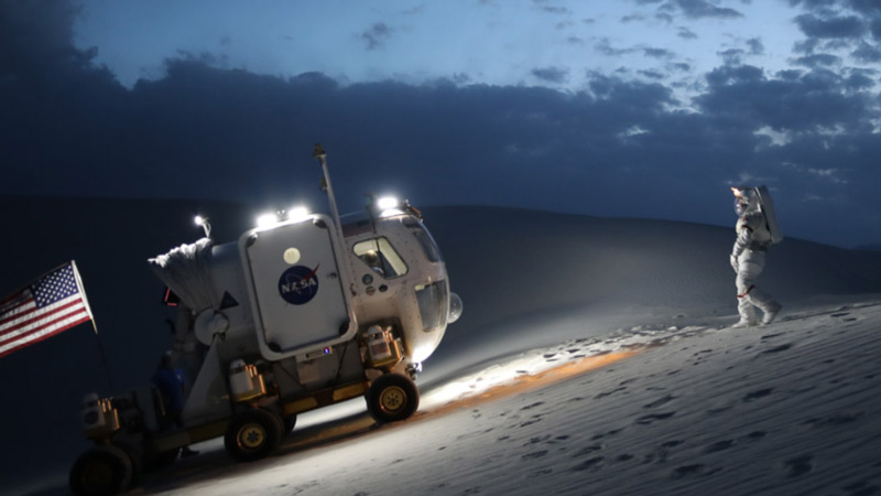 An astronaut walking towards a NASA vehicle in a desert landscape on Earth