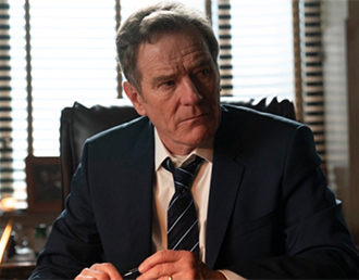 Bryan Cranston wearing a suit and tie, sitting in a chair
